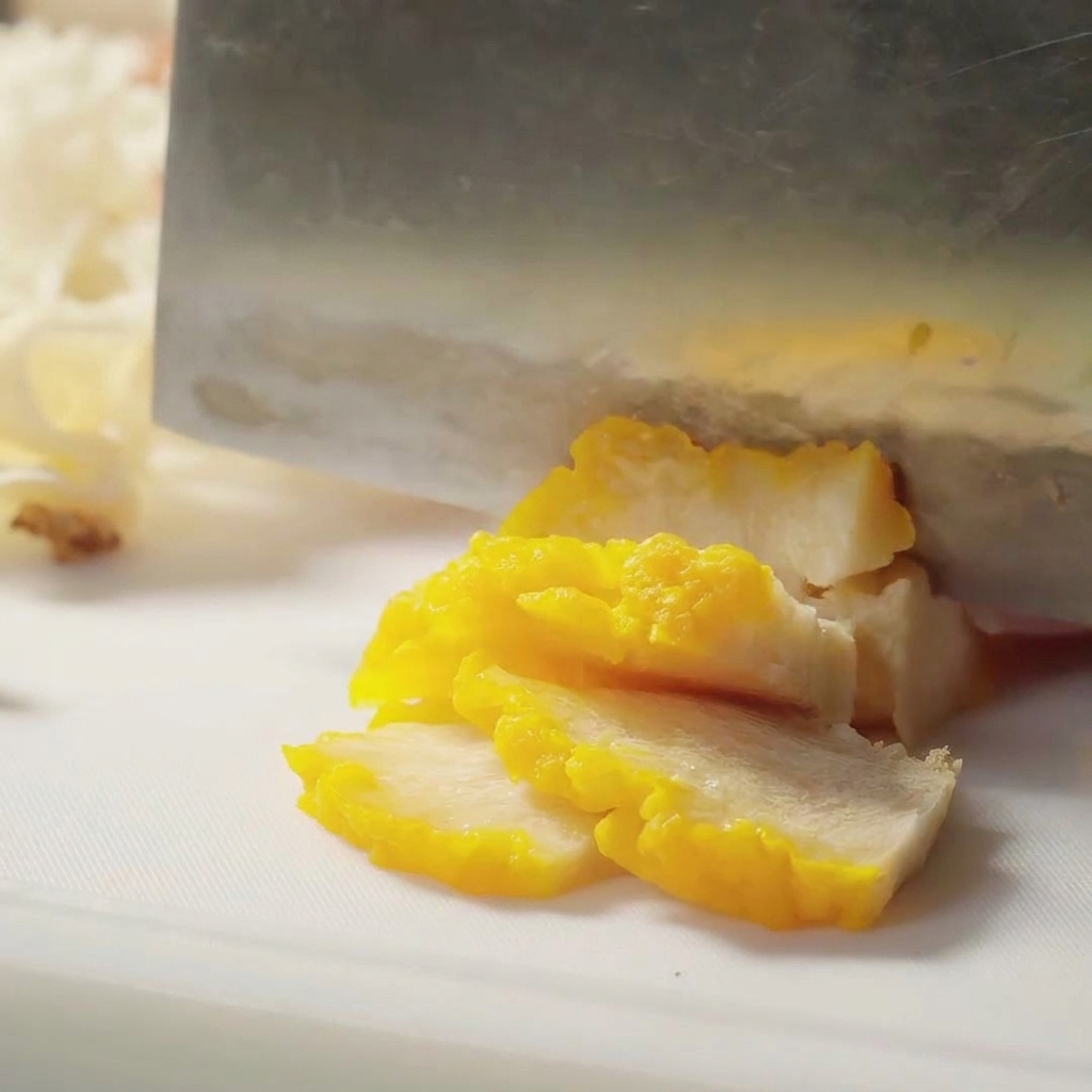 Golden fungus being sliced into thin pieces with a sharp cleaver.