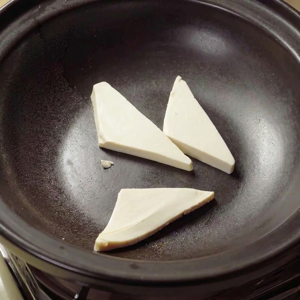 Tofu triangles frying in hot oil inside a clay pot until golden brown.