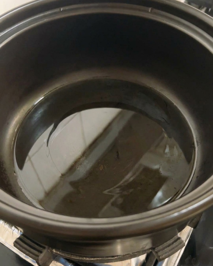 A black pot on a stovetop with a small amount of cooking oil beginning to heat at the bottom.