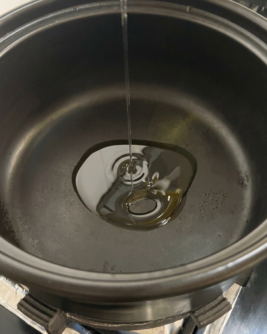 Sliced white button mushrooms being dropped into a black pot containing hot cooking oil.