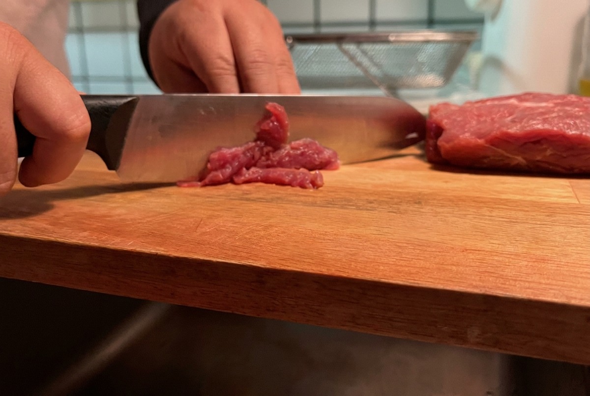 Lean pork being sliced into thin strips on a wooden cutting board.