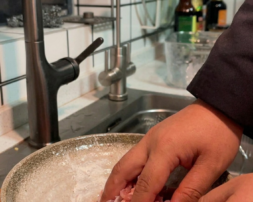Hand mixing seasoned raw pork strips in a bowl to ensure even coating.