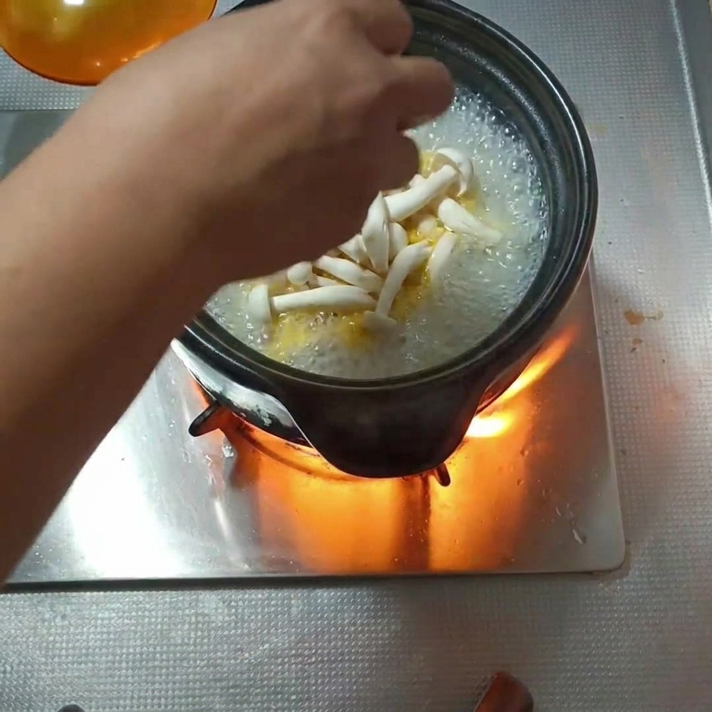 Various types of mushrooms being added to a bubbling clay pot.