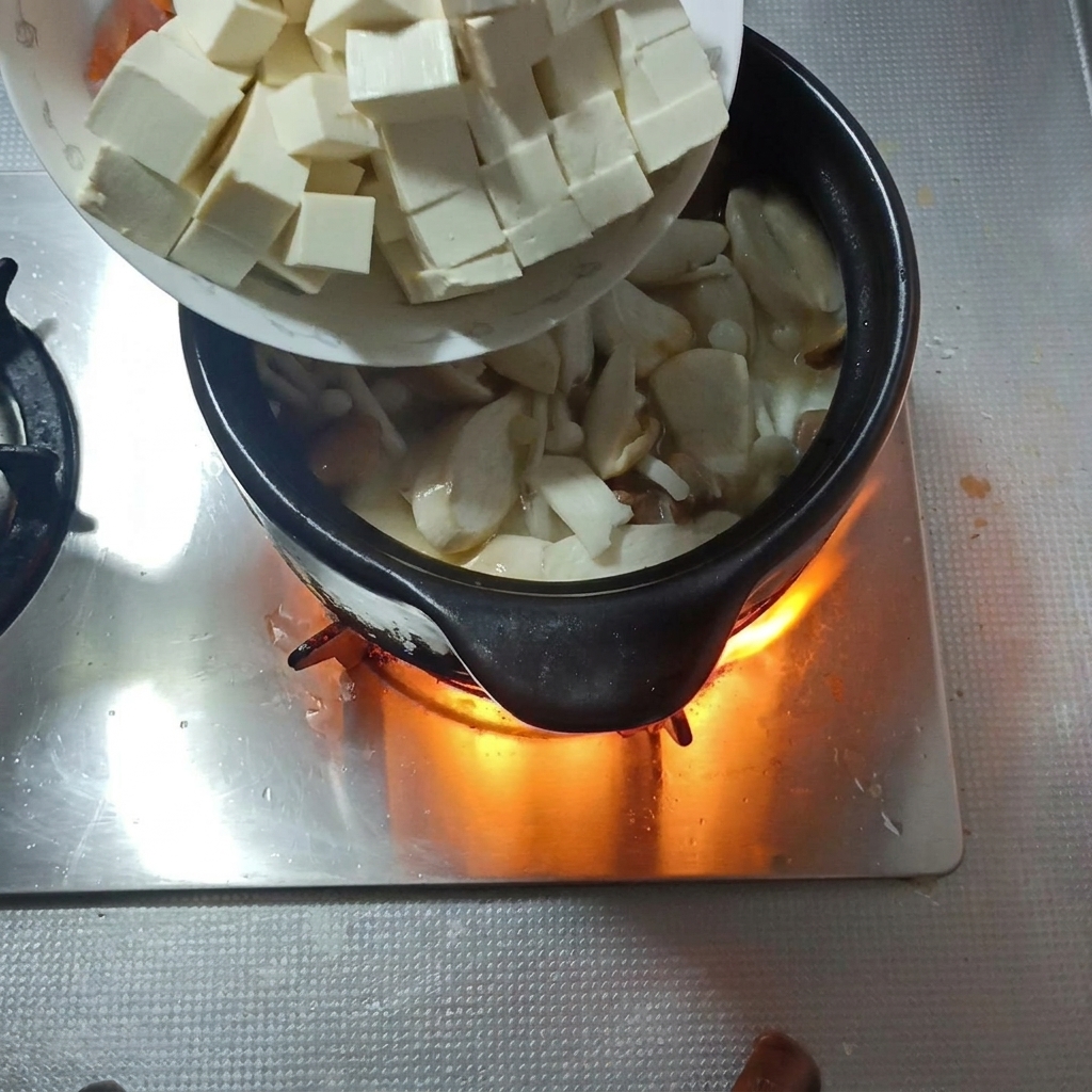 Soft tofu cubes and carrot slices being added to the mushroom soup.