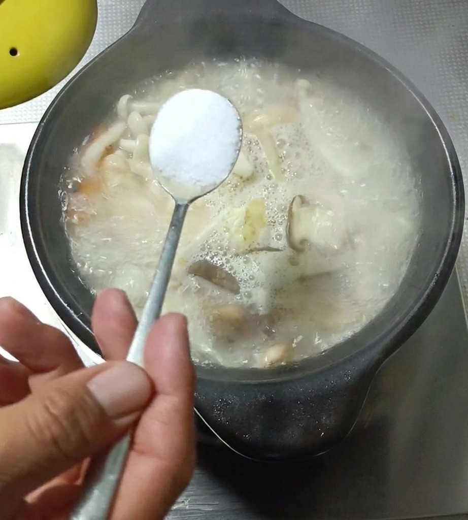 Close-up of a spoonful of seasoning being added to a bubbling pot of mushroom and egg soup.