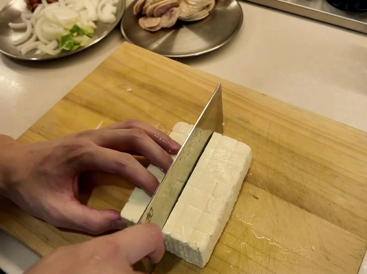 Tofu block being cut into neat slices on a wooden cutting board.