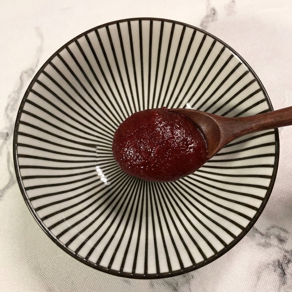 A wooden spoon adding a generous dollop of red Korean chili paste into a bowl with striped patterns.
