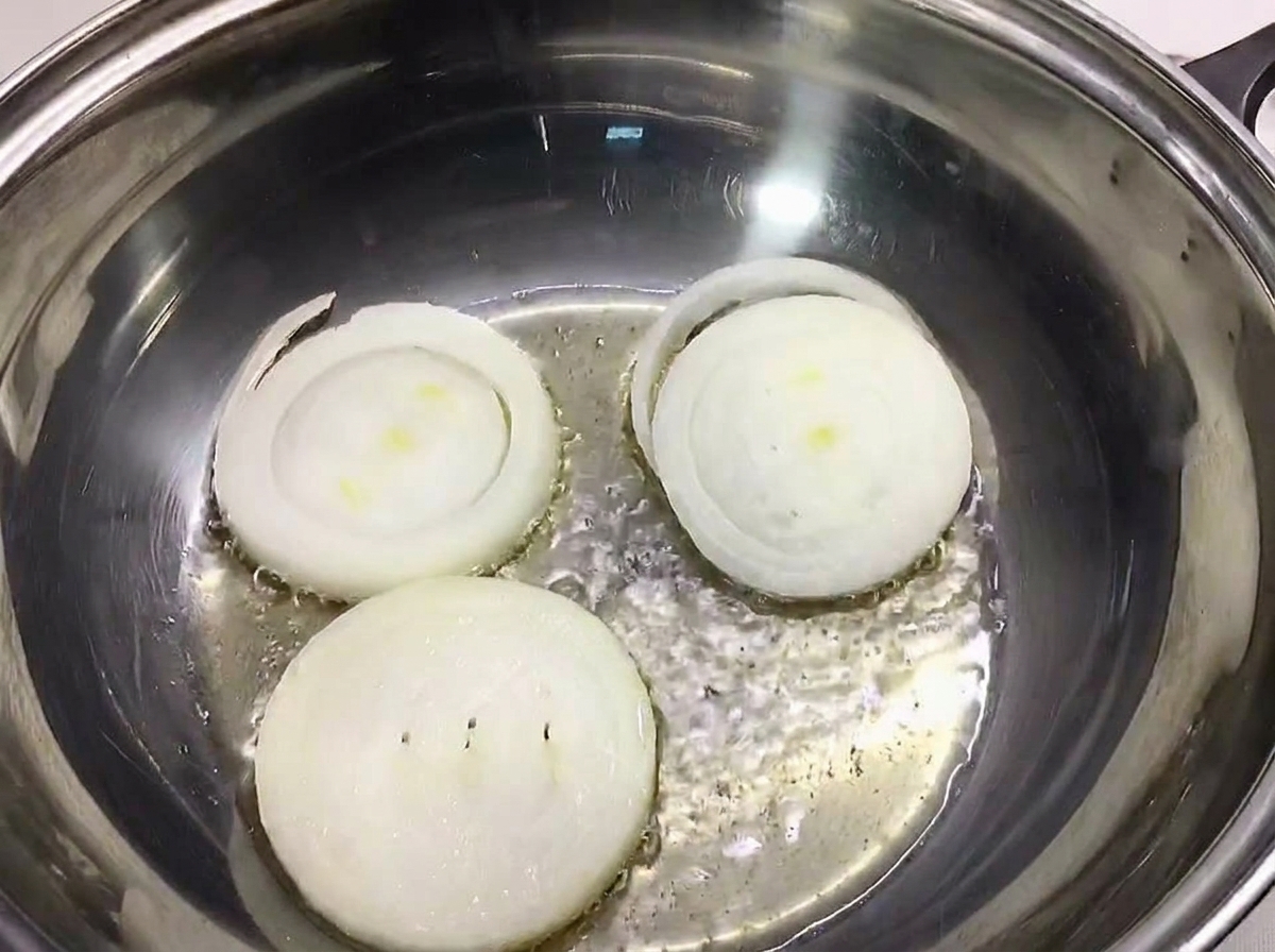 Three thick slices of white onion laid out at the bottom of a stainless steel cooking pot.