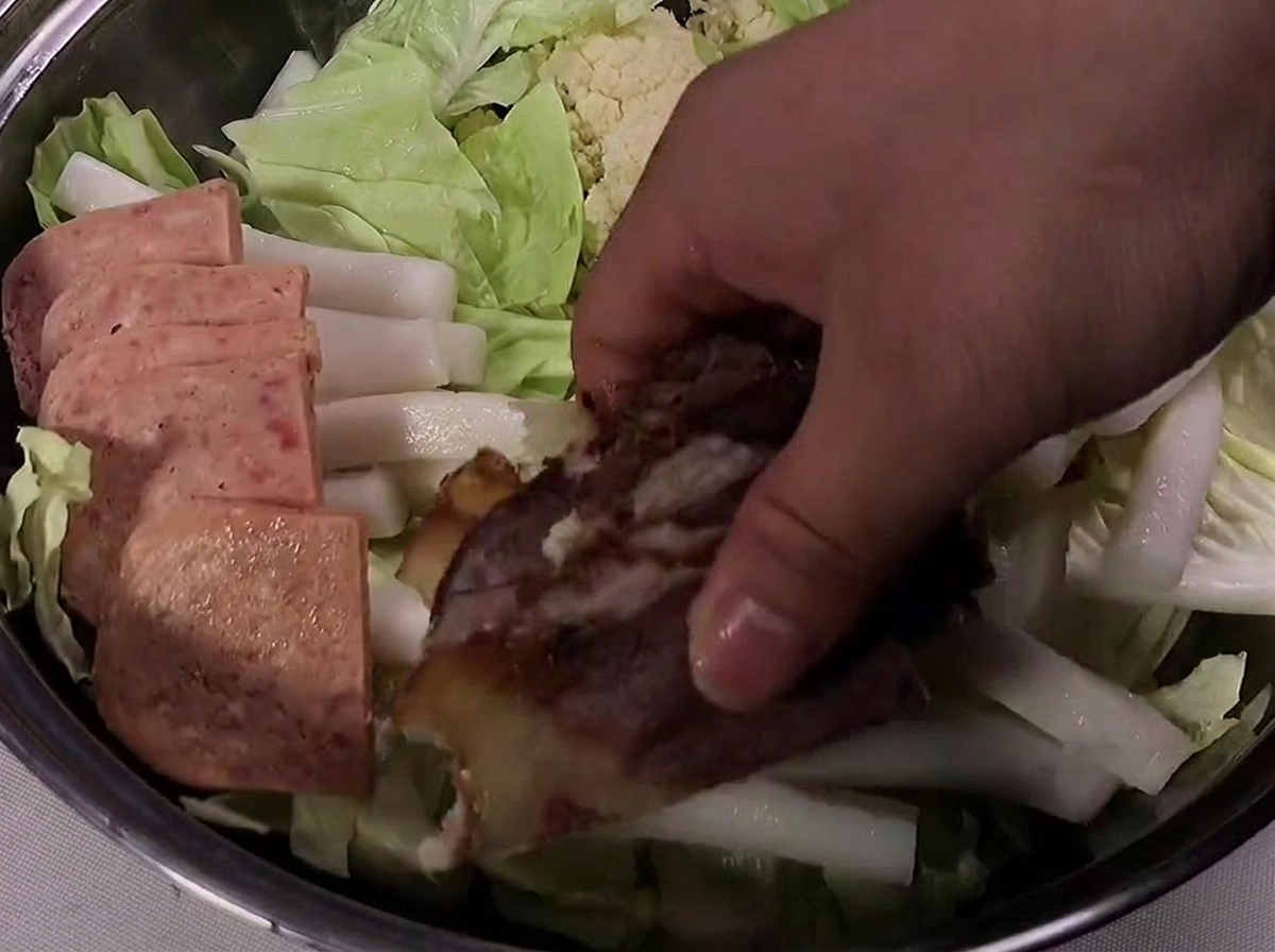 Slices of Spam, cooked beef, and sausage neatly arranged around the edge of the pot.
