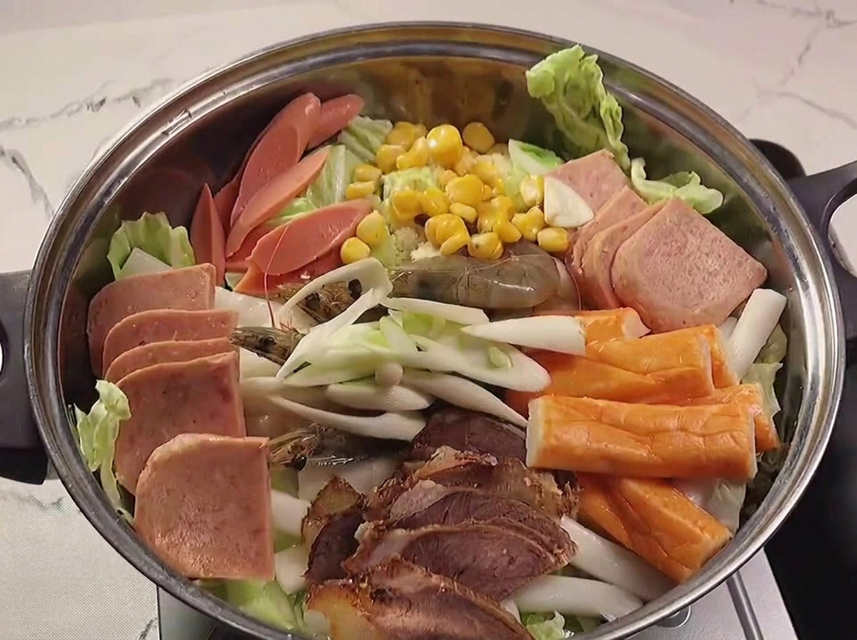 A thick red spicy sauce being drizzled and spread over the assembled ingredients in the pot.