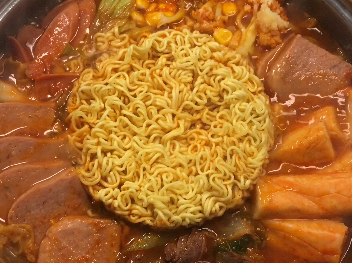 Two squares of golden yellow cheese melting gently on top of the cooked ramen noodles in the pot.