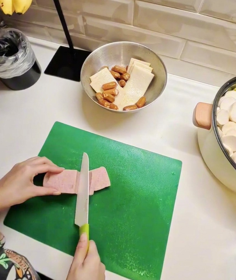 Slices of luncheon meat and fish cakes arranged on a board, showcasing the preparation for the main stew ingredients.