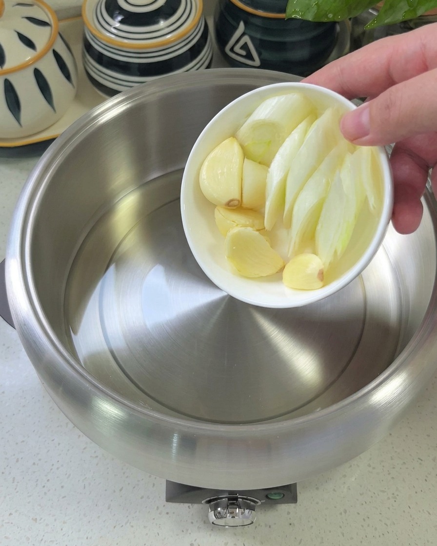 Sautéed garlic, scallions, and red onions in a stainless steel pot, showing a glistening, aromatic base.