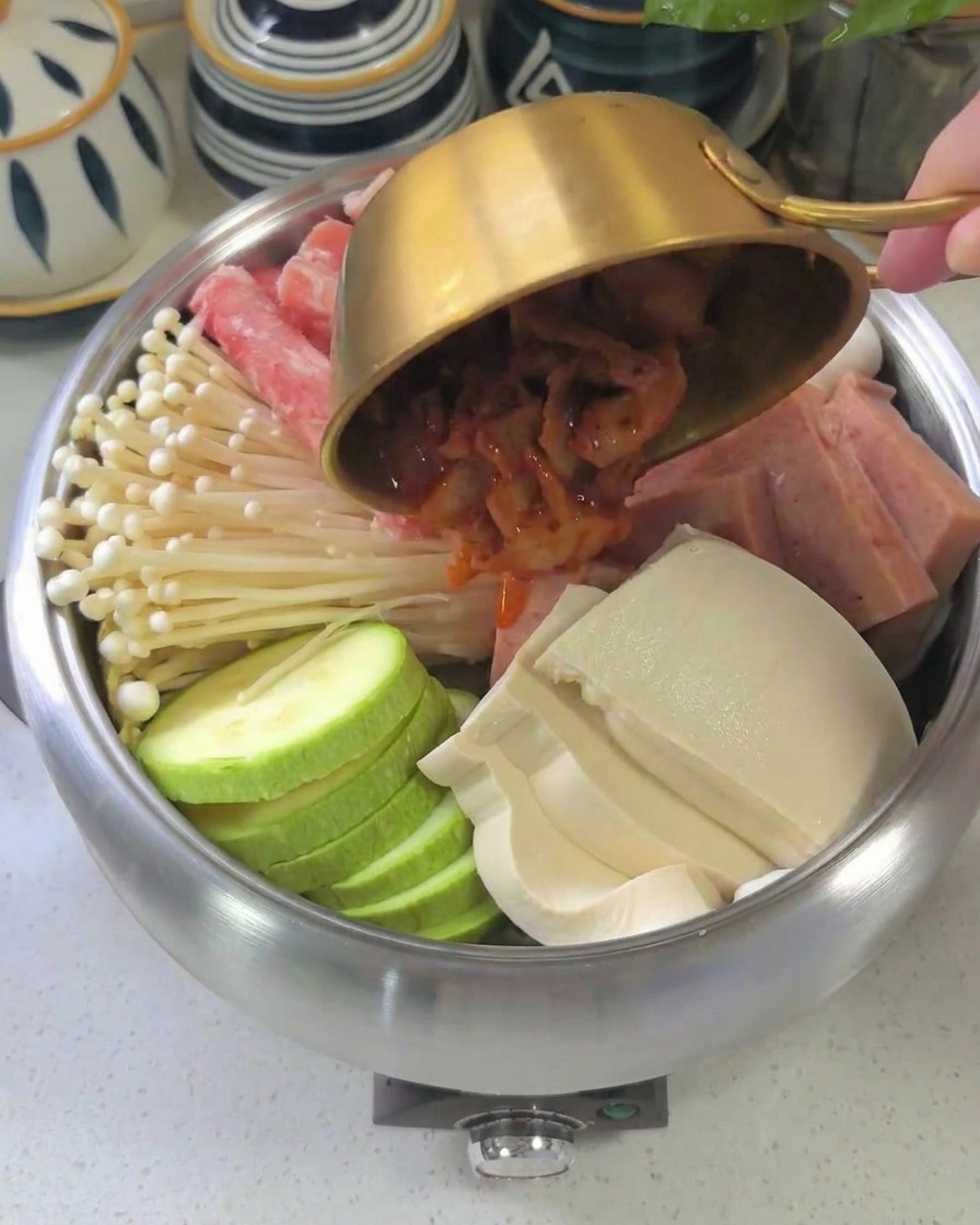The thick, dark red sauce being poured from a bowl over the arranged ingredients inside the pot.