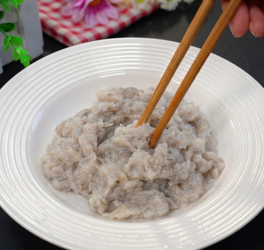Minced shrimp meat being stirred with a pair of wooden chopsticks in a white ceramic bowl.