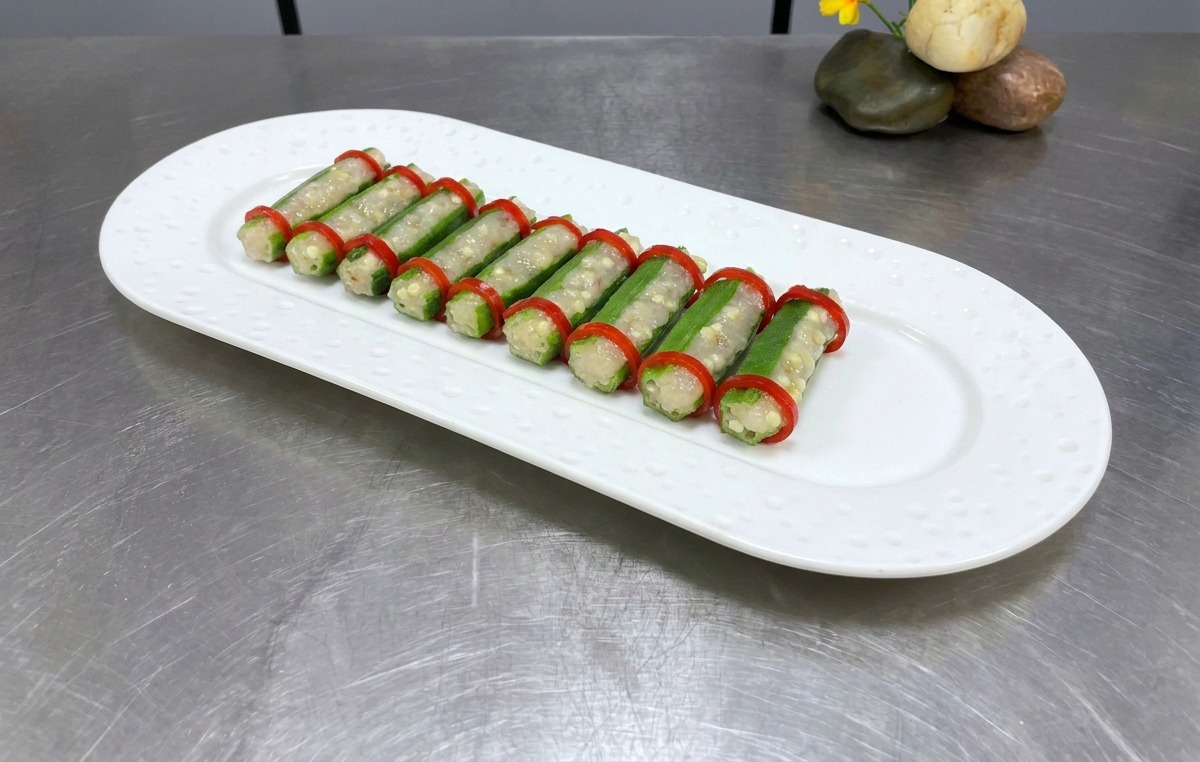 Two neat rows of stuffed okra with red chili rings on a white oval plate, ready for steaming.