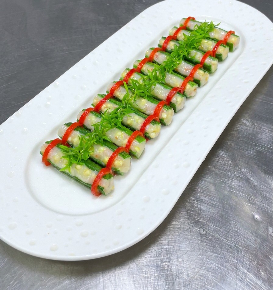 Steamed stuffed okra on a white plate topped with a central row of bright green shredded scallions.