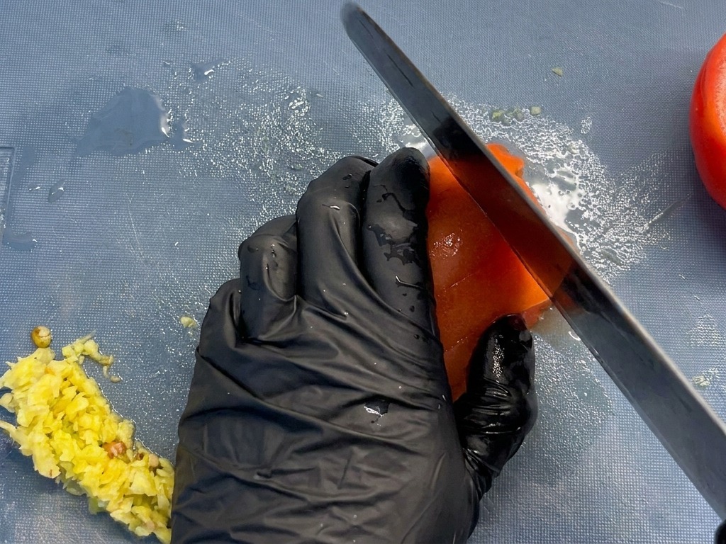 Close-up of a chef dicing a peeled red tomato into uniform chunks on a blue cutting board.