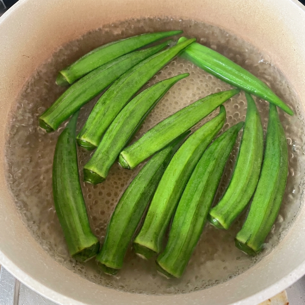 Fresh green okra pods floating in a pot of simmering water.