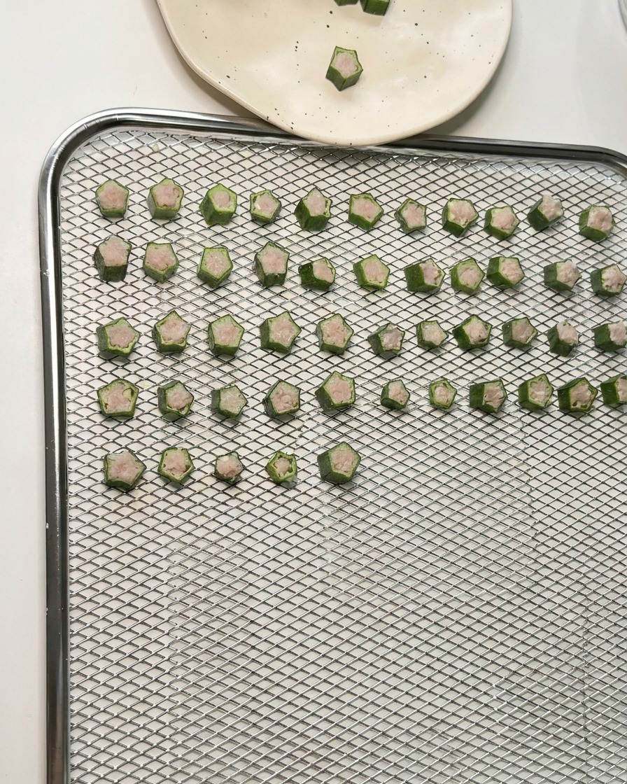 Dozens of star-shaped okra and chicken treats arranged in neat rows on a wire mesh dehydrator tray.