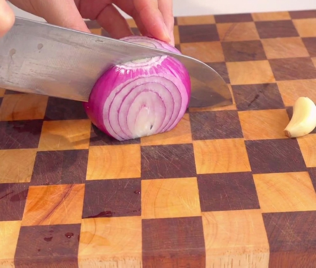 A person finely dicing a red onion into small, uniform cubes on a checkered wooden cutting board.