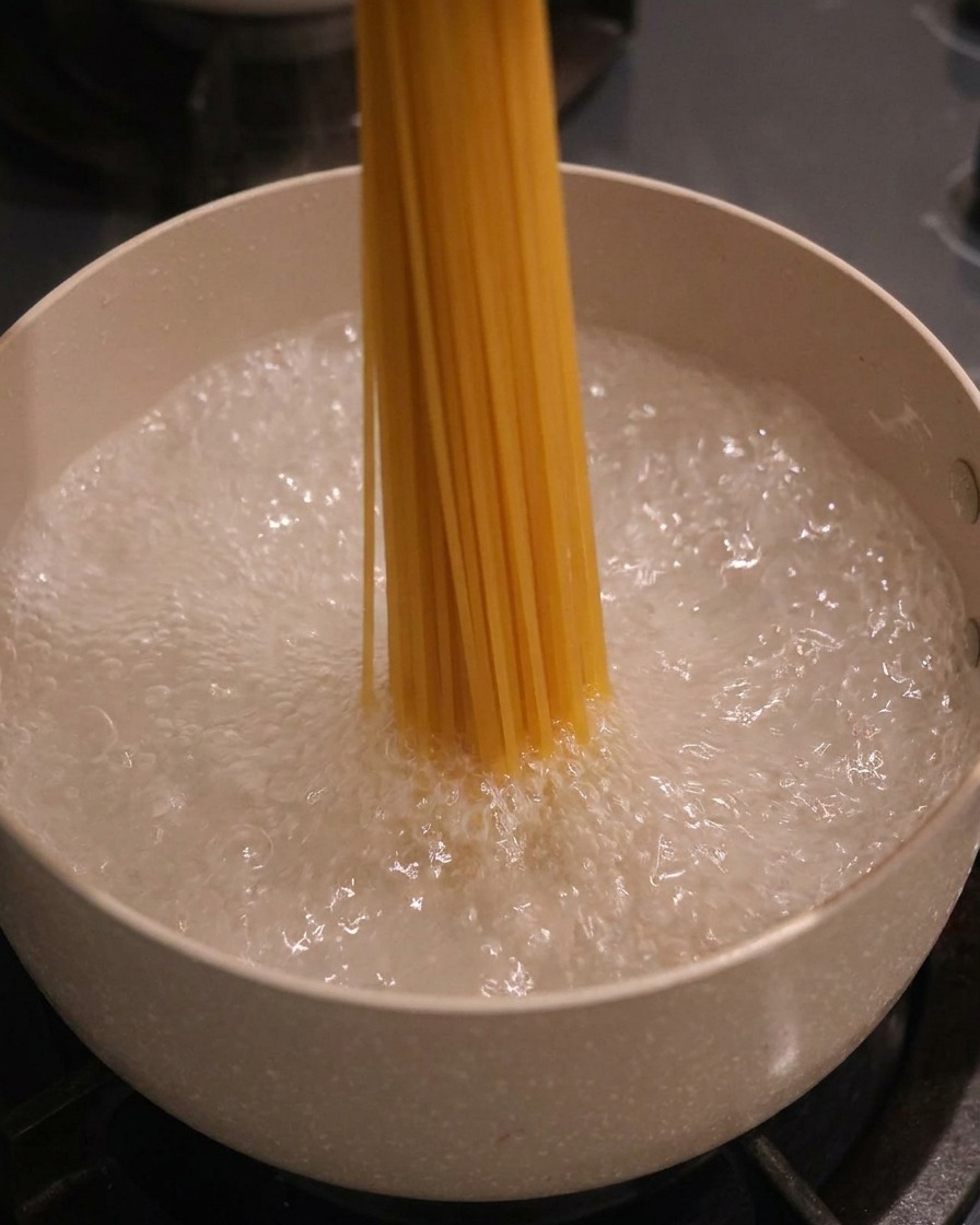 A bundle of dry spaghetti being placed vertically into a pot of boiling, bubbly water.