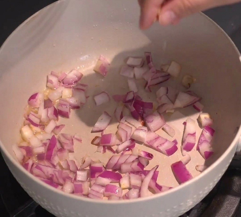 Diced red onions being tossed and sautéed in a light-colored pan on the stovetop.