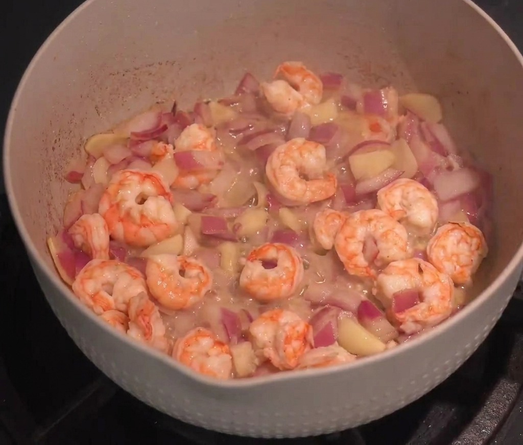 Fresh shrimp being stir-fried with sautéed red onions and sliced garlic in a large pan.