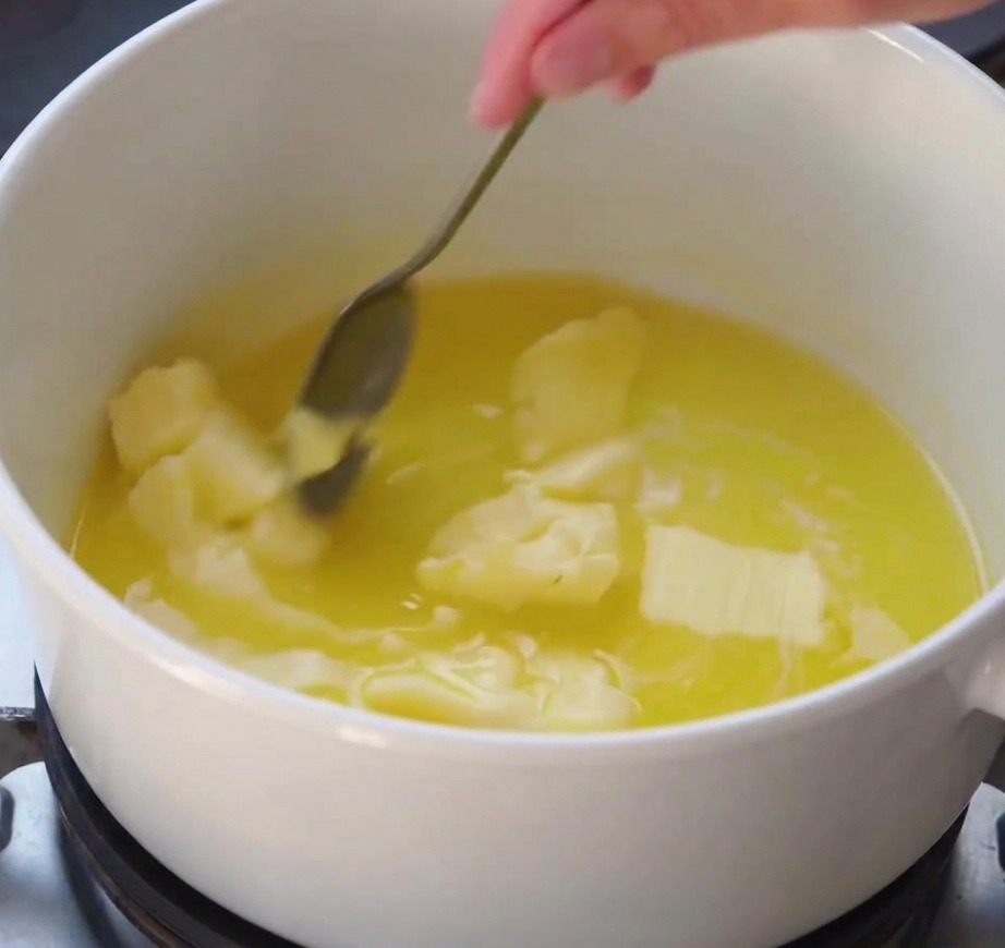 A whisk stirring a smooth white sauce as it thickens in a white pot on a stove