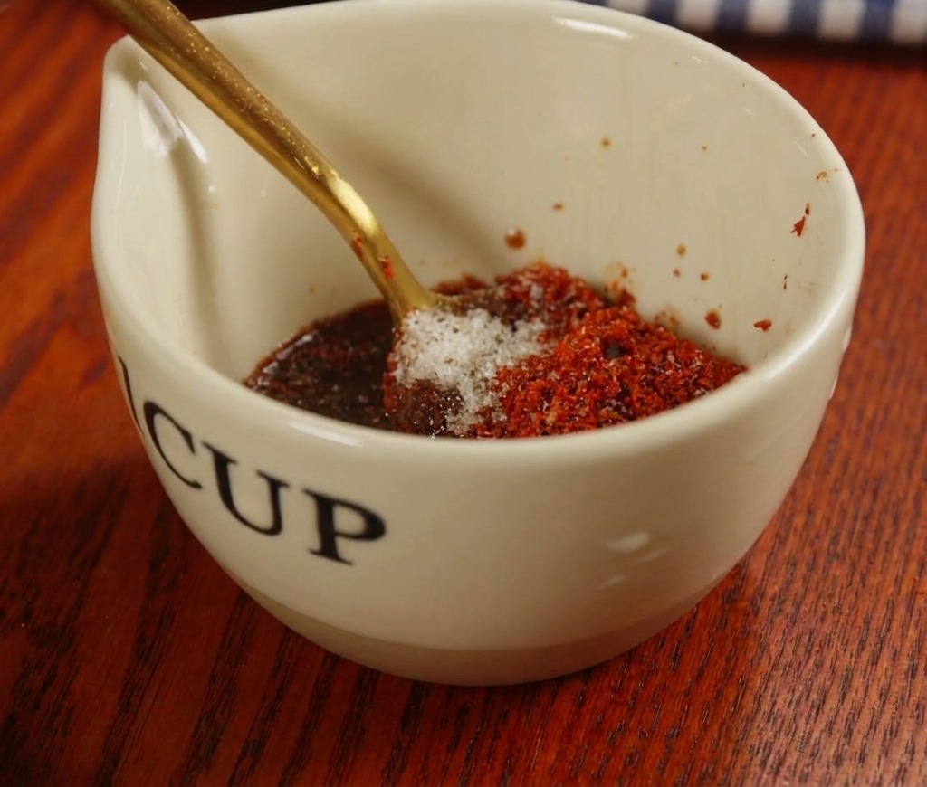 Mixing a red sauce with chili paste and spices in a small ceramic cup with a gold spoon.