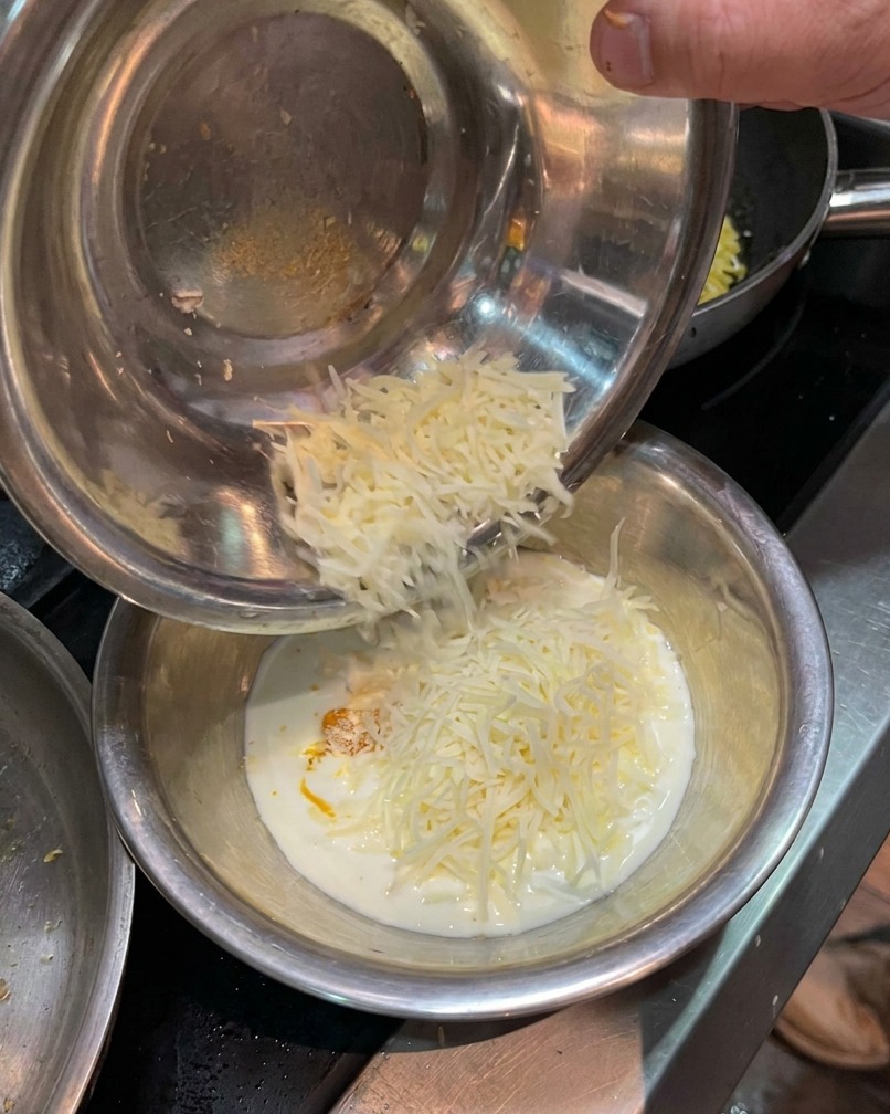 Shredded parmesan cheese being added to a bowl of egg yolk and cream mixture.