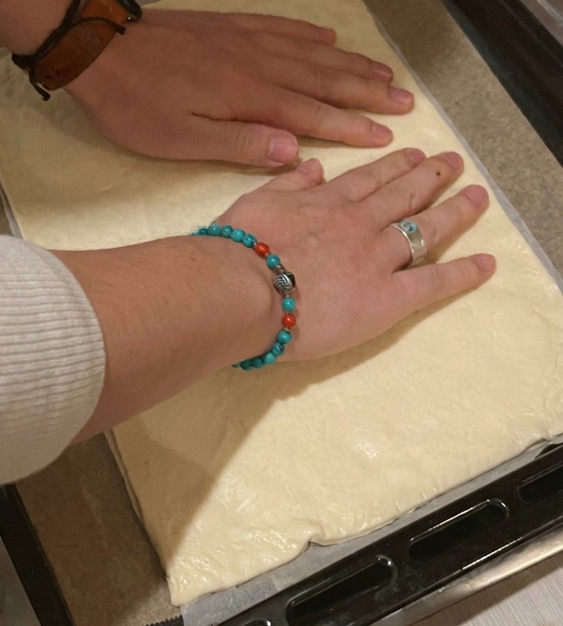 A person laying a rectangular pizza dough base onto a parchment-lined black baking tray.