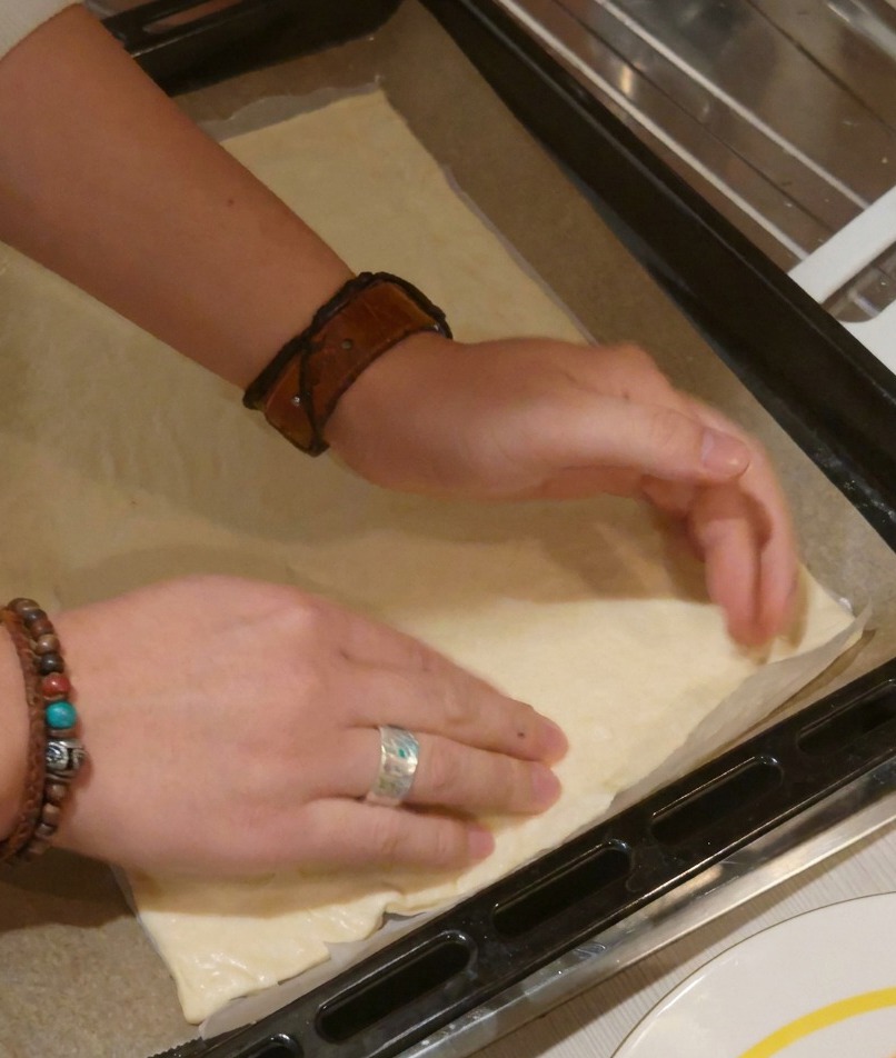 Two hands pressing down on a rectangular pizza dough base to flatten it and define the crust edges.