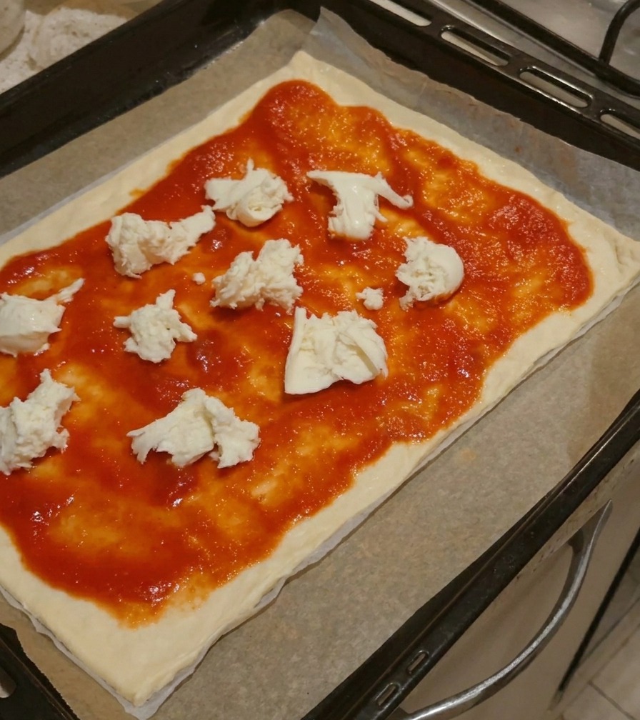 Large chunks of fresh white mozzarella cheese placed on top of tomato sauce on a pizza base.