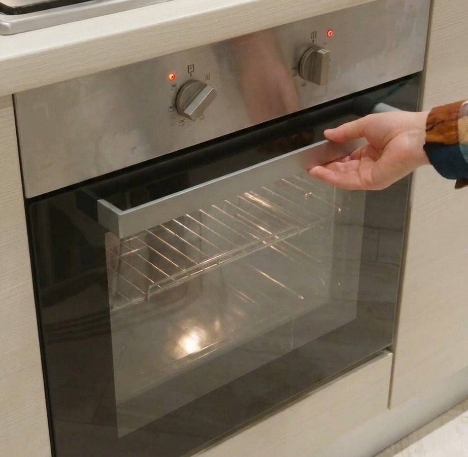 Close-up of a hand adjusting the silver mechanical dials on a stainless steel oven control panel to set the heat and time.
