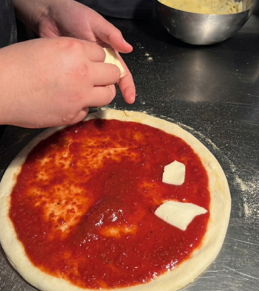 A person placing hand-torn pieces of white mozzarella cheese onto a pizza base already coated with red sauce.