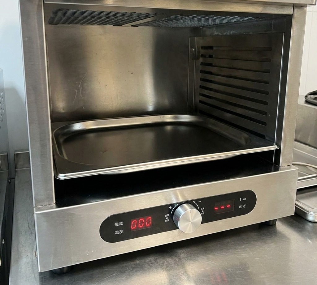 A close-up of a hand adjusting a silver temperature dial on a stainless steel oven with a digital display showing zeros.