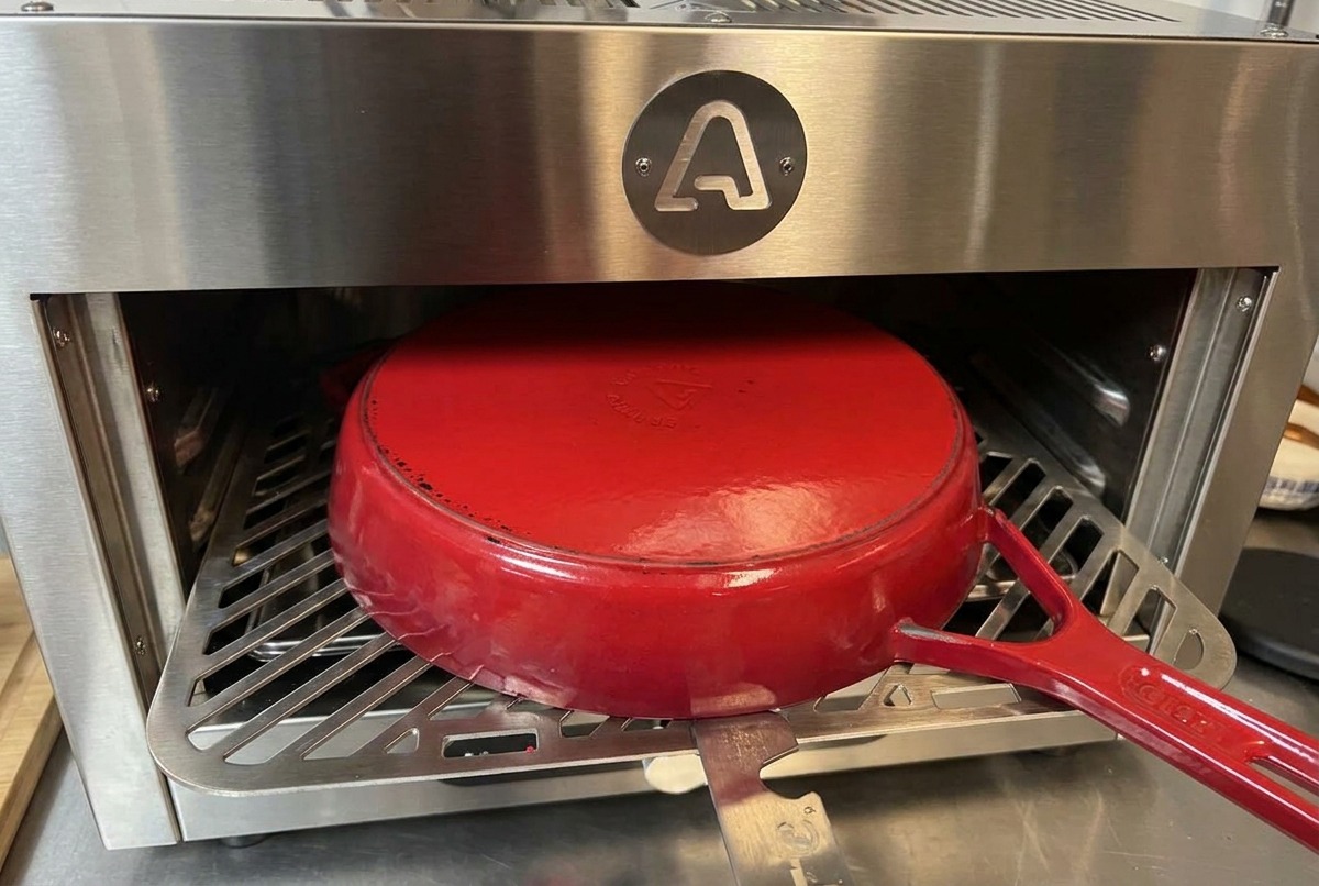 An upside-down red enameled cast iron pot sitting on a metal rack inside a stainless steel oven.