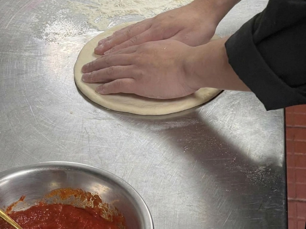 A close-up of hands pressing into a flattened circle of dough to create a raised outer edge.