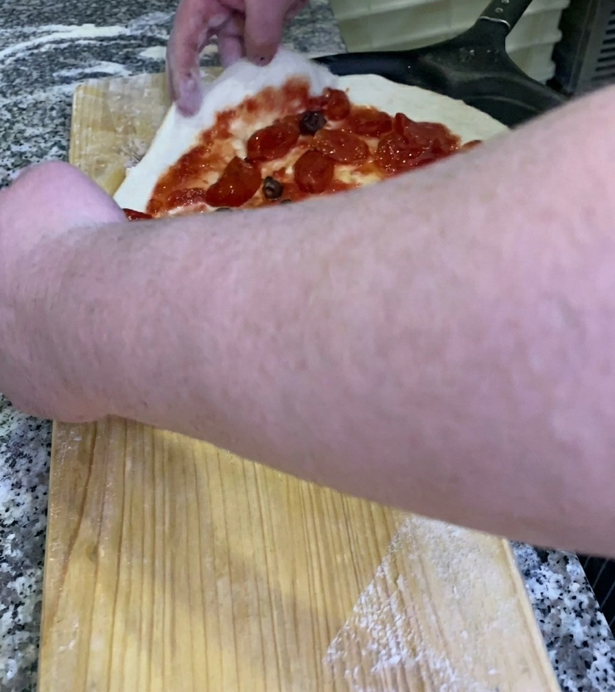 The chef sliding a raw, topped pizza onto a black metal pizza peel from a wooden workbench.