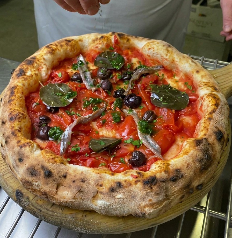 A hand sprinkling fresh green garnish over the center of a baked Marinara pizza.