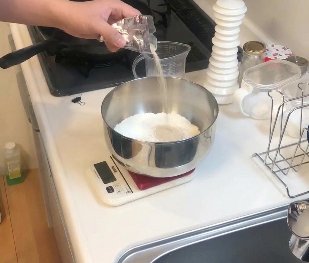 A person pouring white seasoning from a small silver packet into a metal bowl containing white flour.