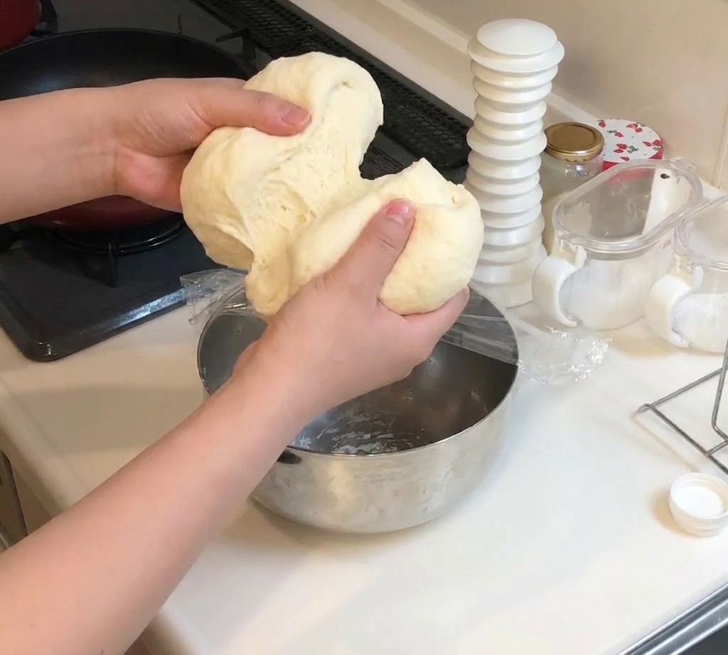 Two hands pulling apart a large piece of soft, stretchy pizza dough to split it into two equal sections.