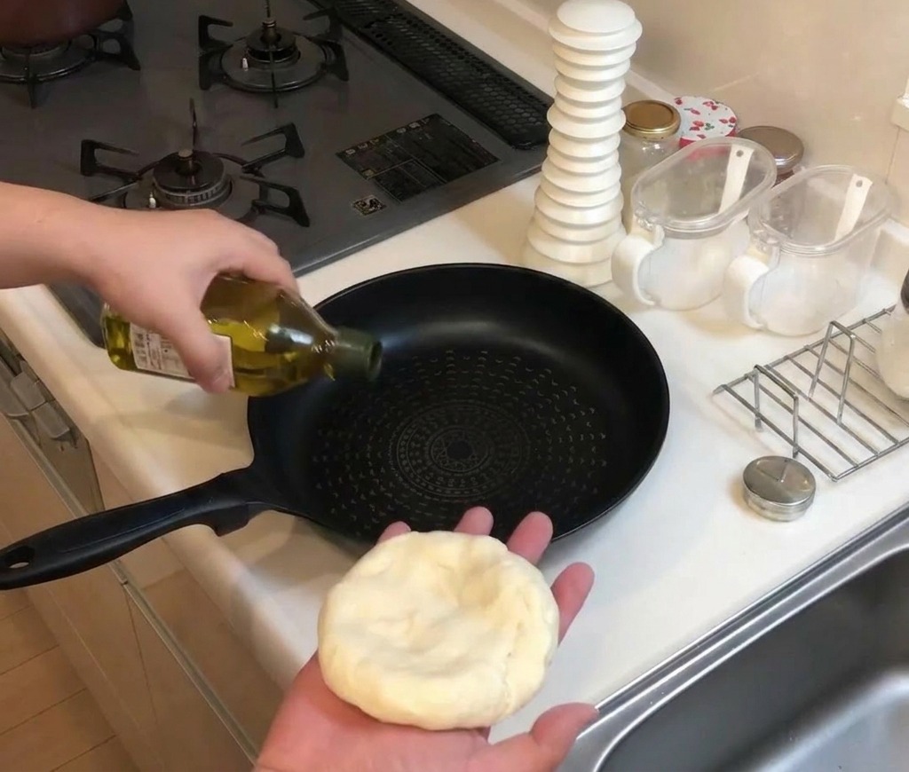 Olive oil being poured from a glass bottle into a black non-stick frying pan on a stovetop.