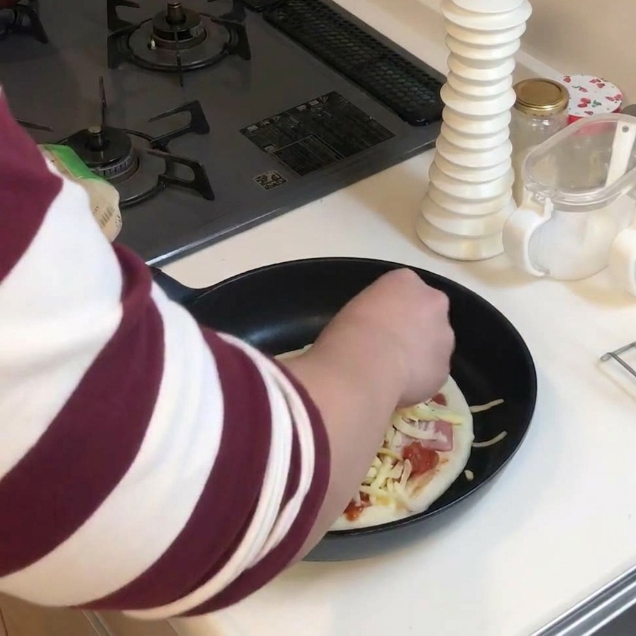 A hand sprinkling a thick layer of shredded yellow and white cheese over a loaded pizza in a pan.