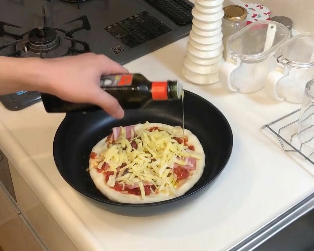 A close-up shot of a hand drizzling olive oil from a dark bottle over a pizza prepared in a pan, topped with shredded cheese and bacon strips.