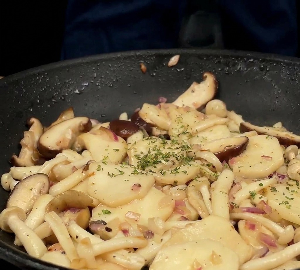 Freshly chopped green parsley being sprinkled over a mixture of sautéed mushrooms and onions in a black pan.