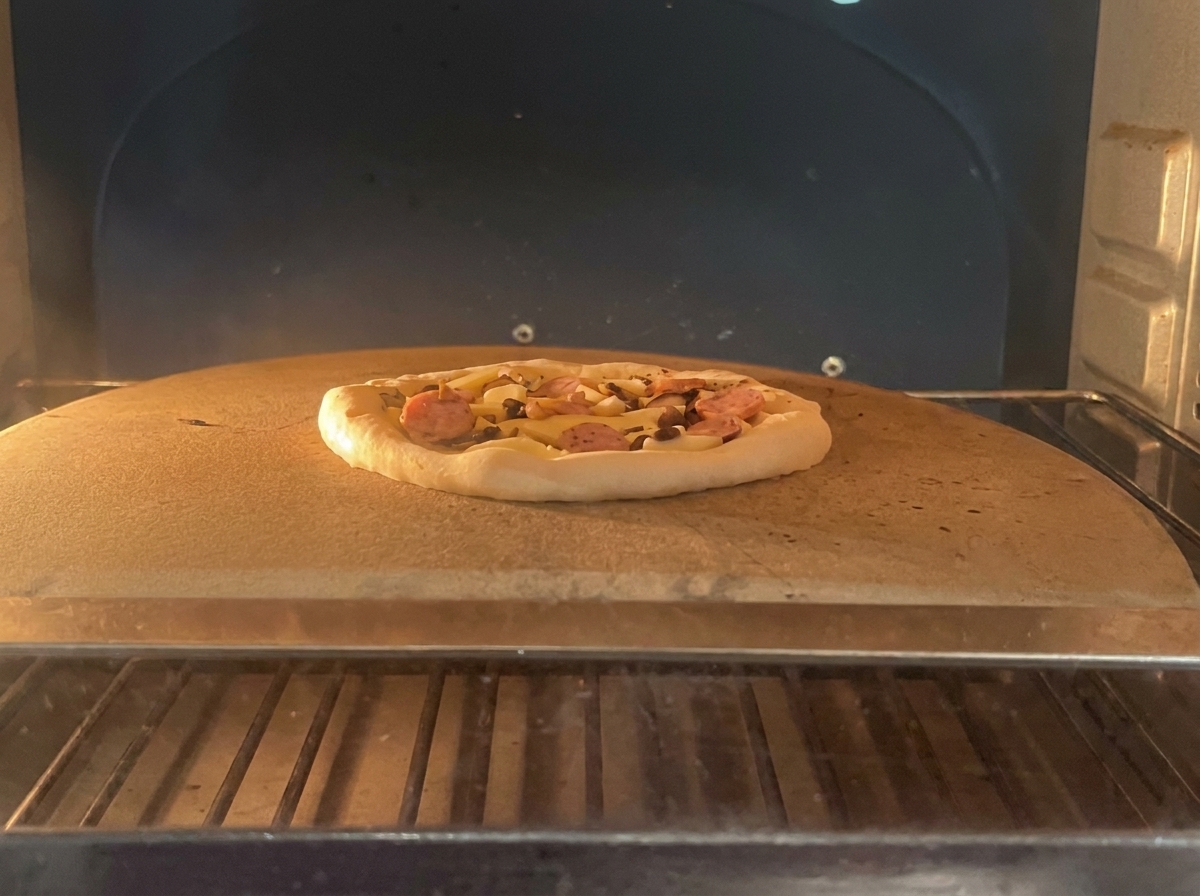 An unbaked pizza with pepperoni and mushroom toppings sitting on a baking stone inside a professional oven.