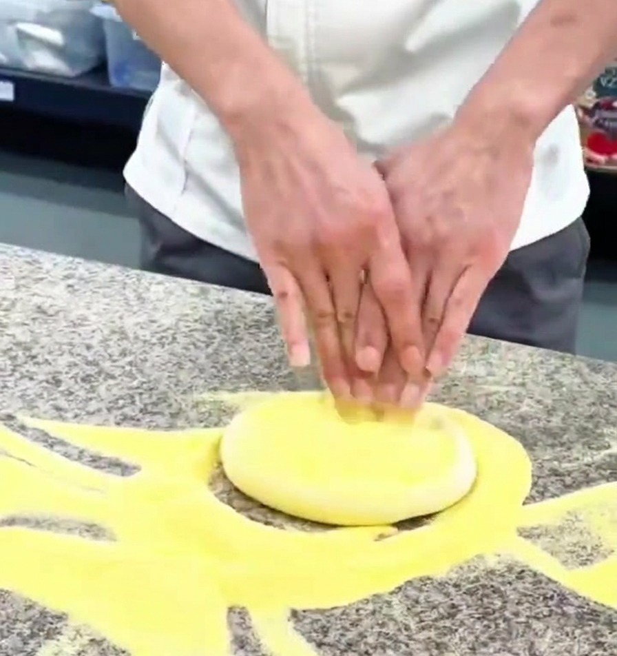 Close up of hands pressing a round piece of pizza dough on a granite counter sprinkled with flour.
