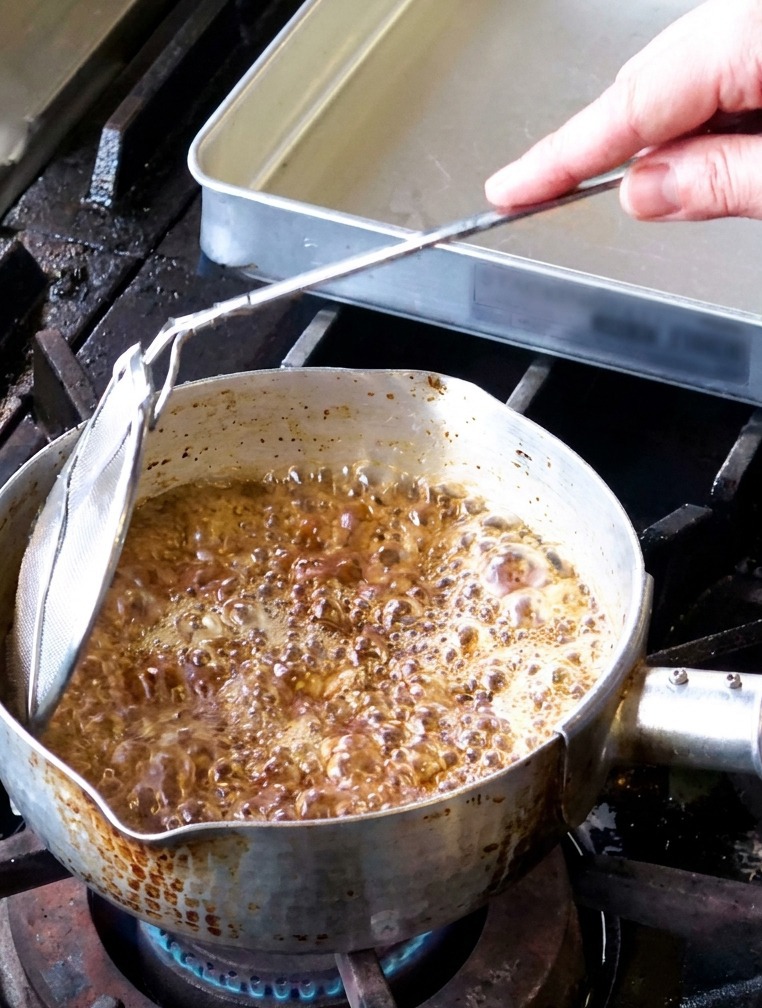 Garlic slices frying in a pot of vigorously bubbling oil with steam rising from the surface.
